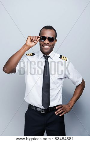 Confident Pilot. Confident African Pilot In Uniform Adjusting His Eyeglasses And Smiling While Stand