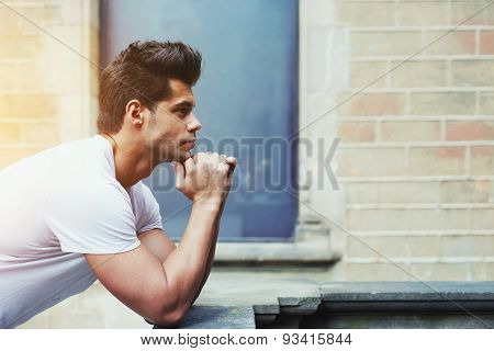Portrait of handsome man resting chin on clasped hands while standing on brick wall background