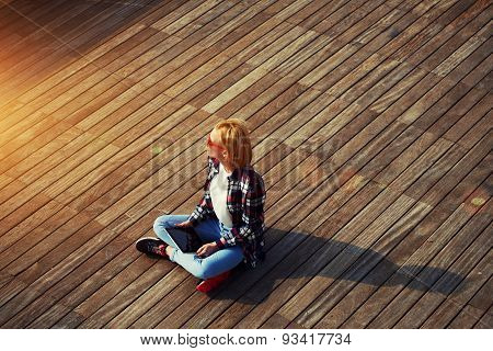 Portrait of a young attractive girl sitting on a wooden floor with a tablet in hands and looks aside