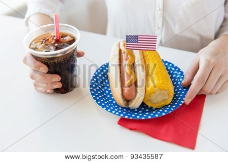 american independence day, celebration, patriotism and holidays concept - close up of woman hands with hot dog and corn holding coca cola drink in plastic cup on 4th july party