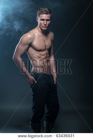 Portrait of a muscular male model against dark background with smoke.