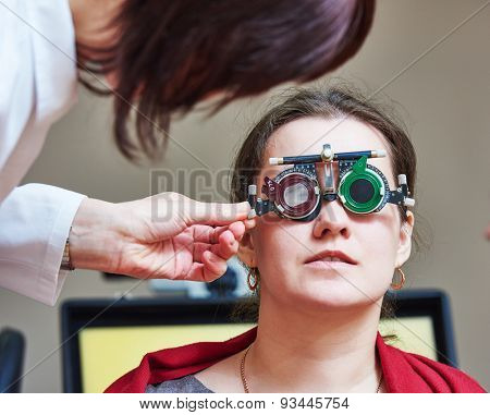 Optometry concept. female doctor ophthalmologist or optometrist helps young woman with phoropter during sight testing or eye examinations in clinic