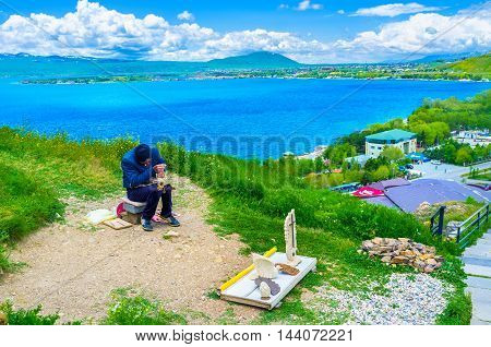 SEVAN ARMENIA - MAY 31 2016: The local sculptor at work on the hill of Sevan Peninsula with the bright blue lake on the background on May 31 in Sevan