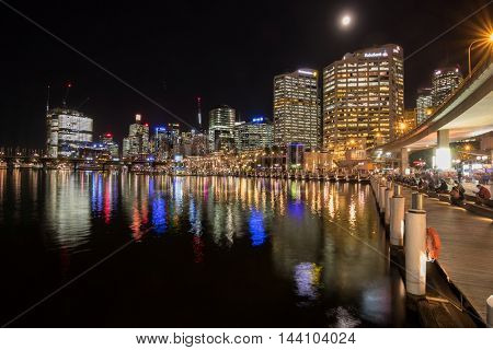 SYDNEY, AUSTRALIA - APRIL, 2016 : People sitting at harbourside promenade with view of Sydney city skyline at night, Cockle Bay Wharf in Sydney, Australia on April 19, 2016. 