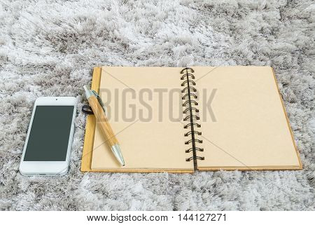 Closeup brown note book with blank space in page brown pen and smart phone on gray fabric capet textured background in top view in work concept