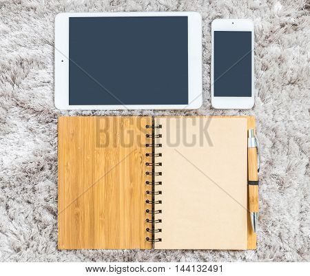 Closeup brown note book with blank space in page brown pen tablet and smart phone on gray fabric capet textured background in top view in work concept