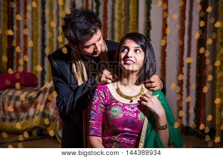 indian husband tying or presenting necklace to his beautiful wife as a diwali gift, indian young couple celebrating diwali festival