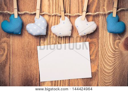 Blank sheet of paper and hand made hearts pinned to brown twine on wooden background
