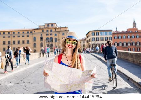 Young female traveler standing with paper map on the crowded bridge in Florence. Vacation in Italy