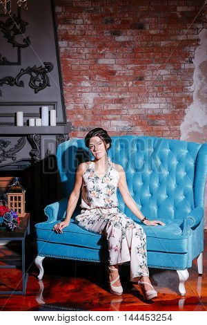 Beautiful woman with blue eyes and curly hair in dress on luxory interer background the fireplace chandelier. blue sofa.
