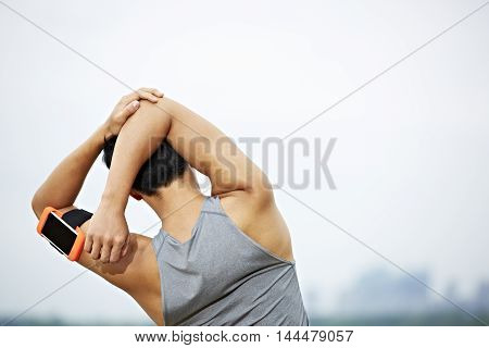 young asian male jogger with fitness tracker attached to arm warming up by stretching arms and upper body before running.