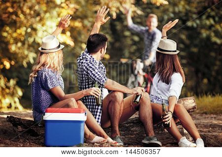 Group of friends is sitting on stump while their friend is comming with bike.