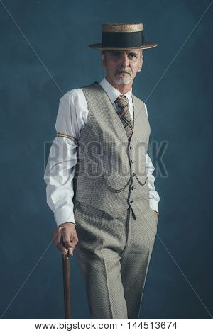 Retro 1920S Dandy In Suit Standing With Cane In Front Of Gray Wall.