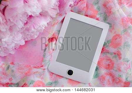 White e-book with a gray screen next to a bouquet of pink flowers on a beautiful gentle background