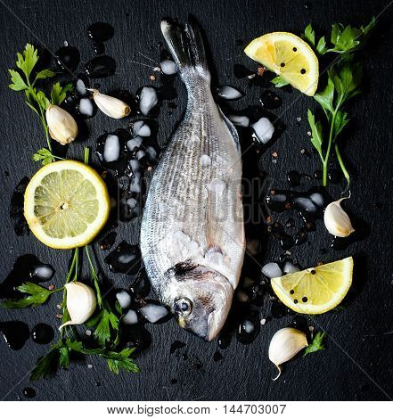 Fresh Fish Orata Over a Black stone with vegetables, lemon and pieces of ice. 