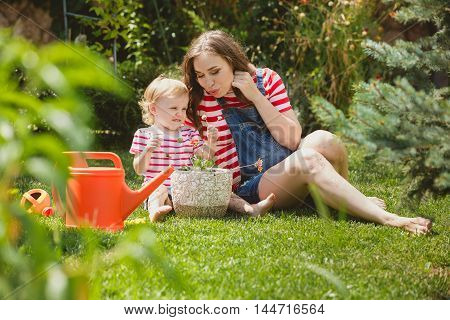 Pregnant woman with little daughter in the summer orchard cearing flower.