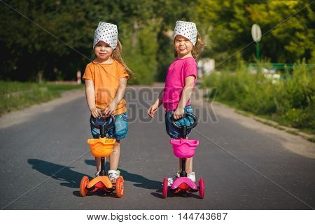 two cute little girls on scooters on the street