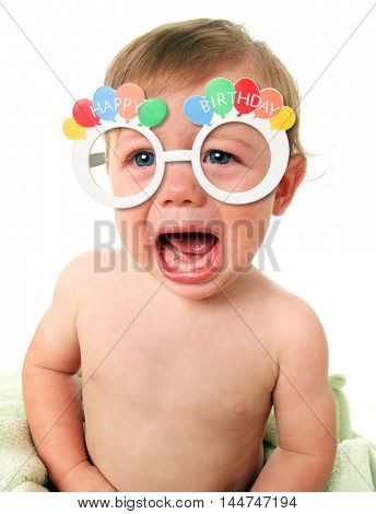 Angry crying baby boy wearing Happy Birthday glasses.