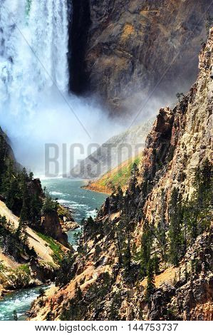 Bottom of Lower Falls in Yellowstone National Park has thunderous spray and crashing water. Yellowstone River curves and twists its way through the steep and high canyon walls.