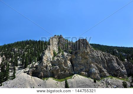 Rugged crevices and ridges rise out of the Gallatin Mountain Range in Montana. Sunny blue sky above.