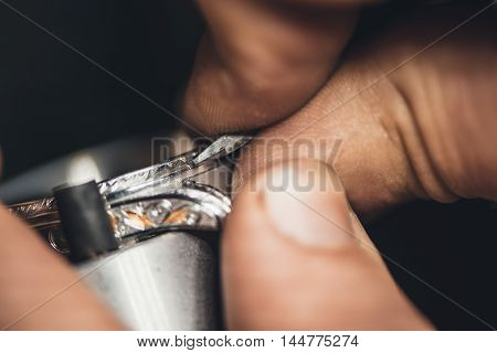 Closeup of a jeweler using tools to shape a silver ring while working at a bench in his workshop