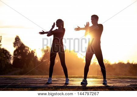 Two silhouettes of young healthy man and woman exercising at sunset. Fitness or running workout outdoors
