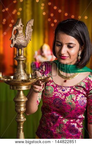 Indian young and beautiful girl in traditional wear lighting oil lamp or samai with diya and celebrating ganesh festival or Diwali or deepavali. Indian girl hands holding oil lamp indoors.