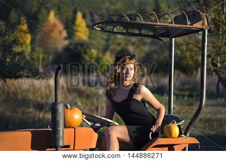 Young female sitting on tractor in rural landsape in autumn with pumpkins