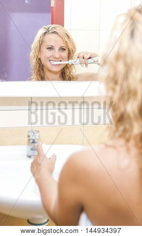 Caucasian Woman Brushing Her Teeth With Modern Electric Toothbrush in Bathroom. Vertical Image