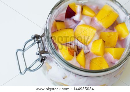 Fresh nectarine slices and creamy yogurt in a glass jar top view
