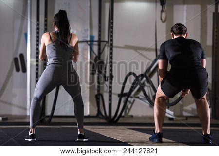 young fit sports couple working out in functional training gym doing  battle ropes cross fitness exercise