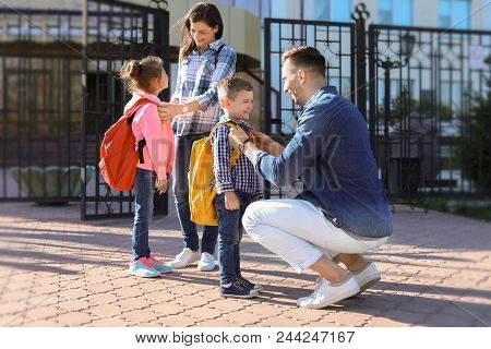 Young Parents Saying Goodbye To Their Little Children Near School