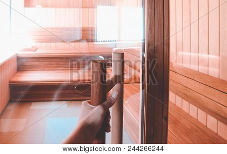 Luxury Wooden Bathhouse With A Window, Sunlight, Hand On The Handle. Elegant Sunny Wooden Sauna Inte