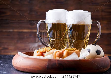 Photo Of Two Mugs Of Beer And Hot Dogs On Wooden Tray With Football On Wooden Background