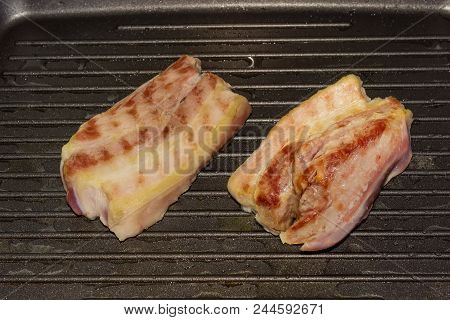 Fragment Of Grill Pan With Two Slices Of The Streaky Bacon During Grilling Closeup At Selective Focu
