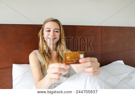 Young Woman Sitting In Bed With Gold Debit Card And Smling, Sitting In Bed. Concept Of Payment Thing