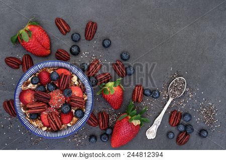 Healthy breakfast super food concept with fresh berry fruit, nuts, chia seeds and granola with foods high in protein, anthocyanins, antioxidants, minerals and vitamins on slate background, top view.