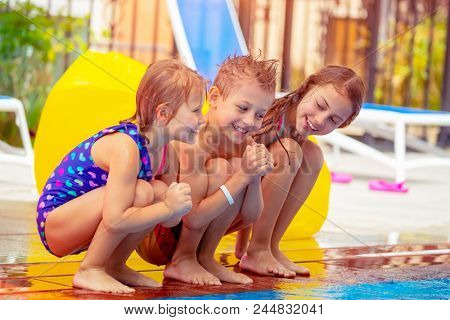 Three happy kids sitting near the pool, having fun in aqua park, best friends with pleasure spending time in summer camp together