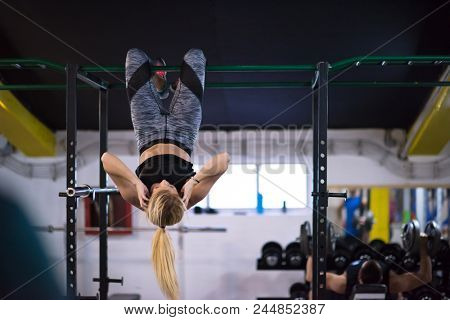 athlete woman doing abs exercises hanging upside down on horizontal bar at cross fitness gym