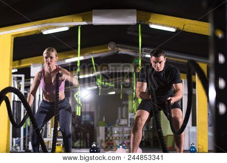 young fit sports couple working out in functional training gym doing  battle ropes cross fitness exercise