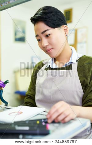 Portrait Of Young Asian Woman Drawing Sketches Sitting At Table In Glassworking Studio
