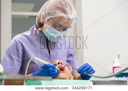 Dentist In The Process. / A Dentist Uses Ultrasound And A Saliva Ejector To Clean A Patient’s Dental