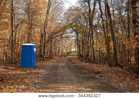 A Lone Outdoor Portable Potty Is Left Standing Along A Trail In An Autumn Woods.