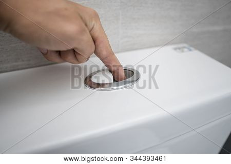 Close Up Of Finger Pushing A Flush Toilet Button For Cleaning A Toilet.