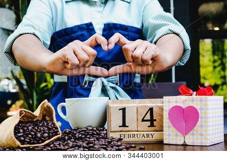Woman Hand Show Heart Shap With Gift Box, 14 February Wooden Calendar, Coffee Cup And Coffee Beans. 
