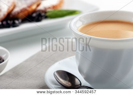 A Cup Of Coffee With Milk And A Plate With A Pancakes Is On The Table.