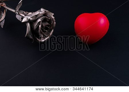A Thin Bronze Rose Made By Forging From Metal. Red Volumetric Heart Nearby.