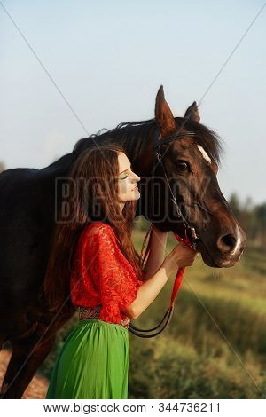 Gypsy Girl Rides A Horse In A Field In The Summer. A Woman With Long Hair Strokes And Caresses A Hor