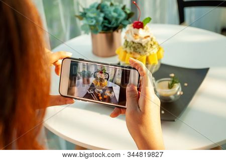 An Asian Woman Takes A Picture Of An Ice-mango In A Cafe And Prepares To Upload It To A Social App.