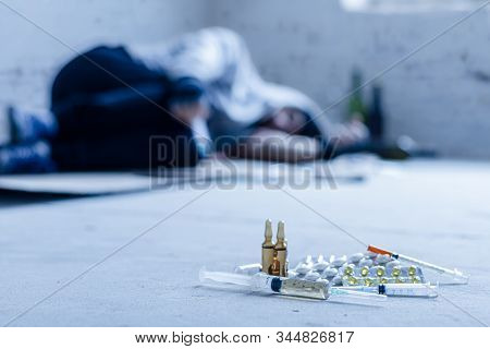 Closeup Syringes, Ampoules And Pills. On Background Young Junkie Homeless Addict Man Is Sleeping Aft